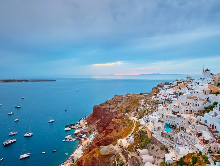 Santorini cliffside with white buildings and boats in the sea, ideal for car rental sightseeing trips.