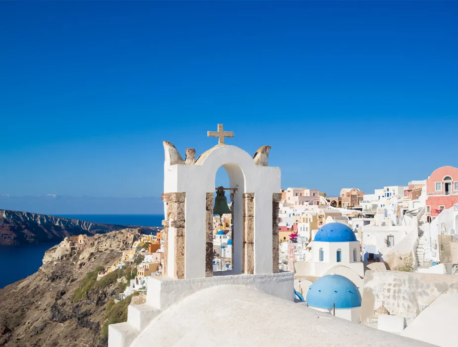 Santorini town with white buildings and blue domes by the sea under clear sky.