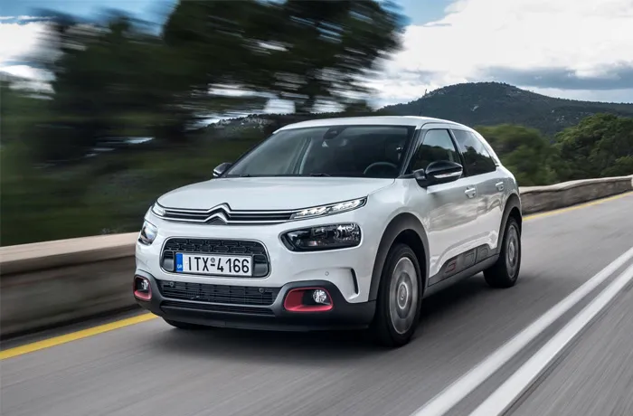Ενοικίαση αυτοκινήτου Citroën C4 Cactus οδηγώντας σε αγροτικό δρόμο με λόφους και δέντρα στο βάθος.