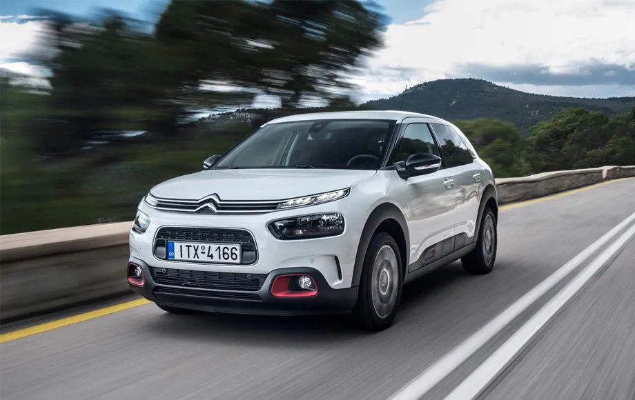 Închiriere mașină Citroën C4 Cactus pe un drum pitoresc cu dealuri și copaci în fundal.