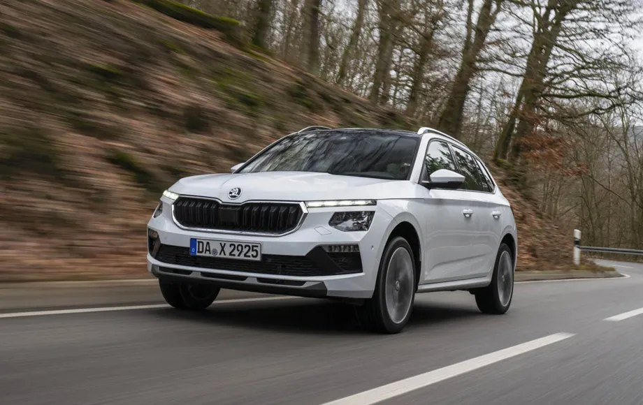 SUV alb Skoda Karoq de închiriat conduci pe un drum șerpuit printr-o zonă împădurită.