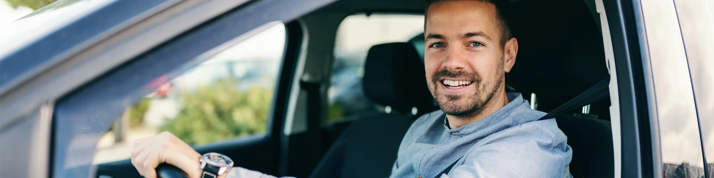 Man smiling while sitting in a rental car with a seatbelt fastened, ready to drive.